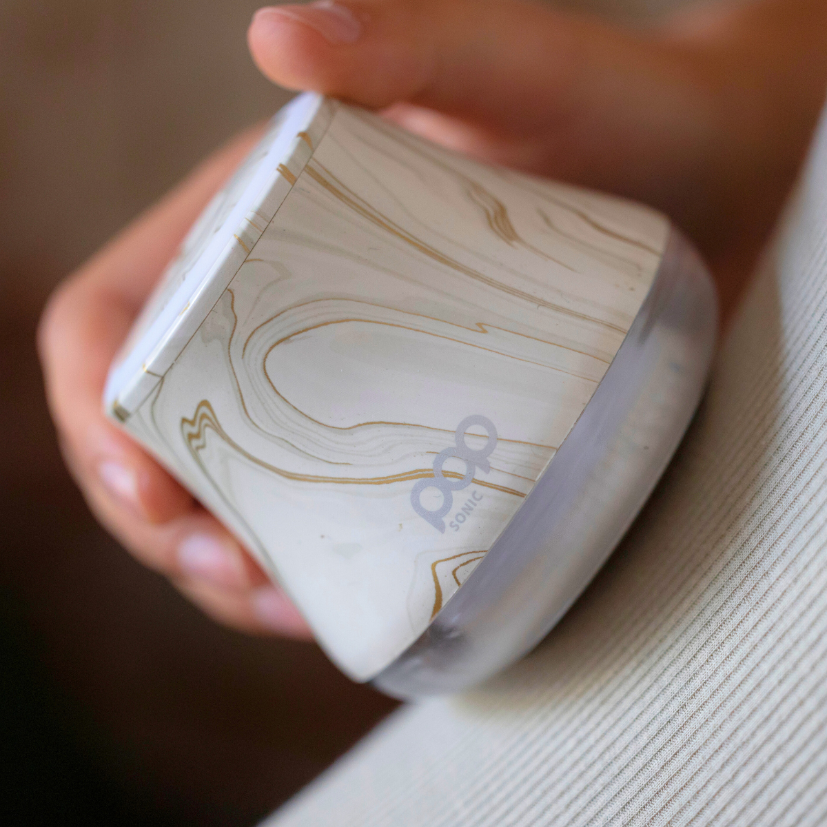 Hand holding Fabric Shaver with marbled design onto a beige shirt