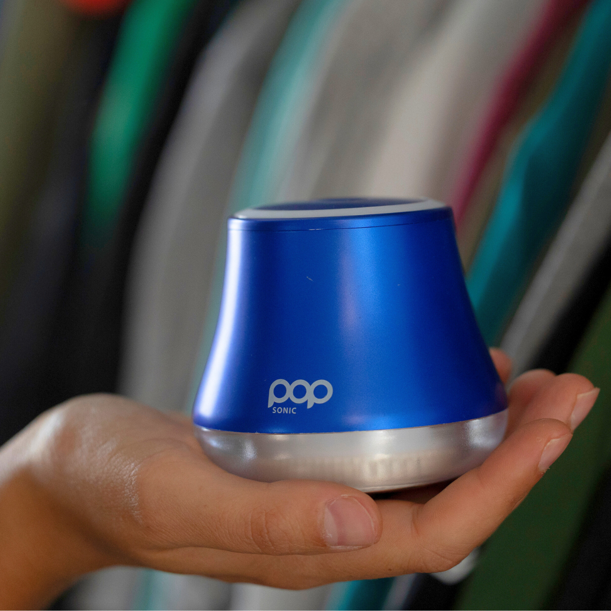 Blue and silver Fabric Shaver held in a hand against a blurred background