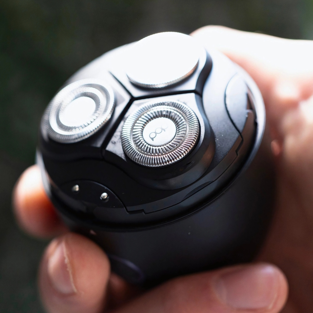 Close-up of a black electric shaver held in a hand with a blurred background