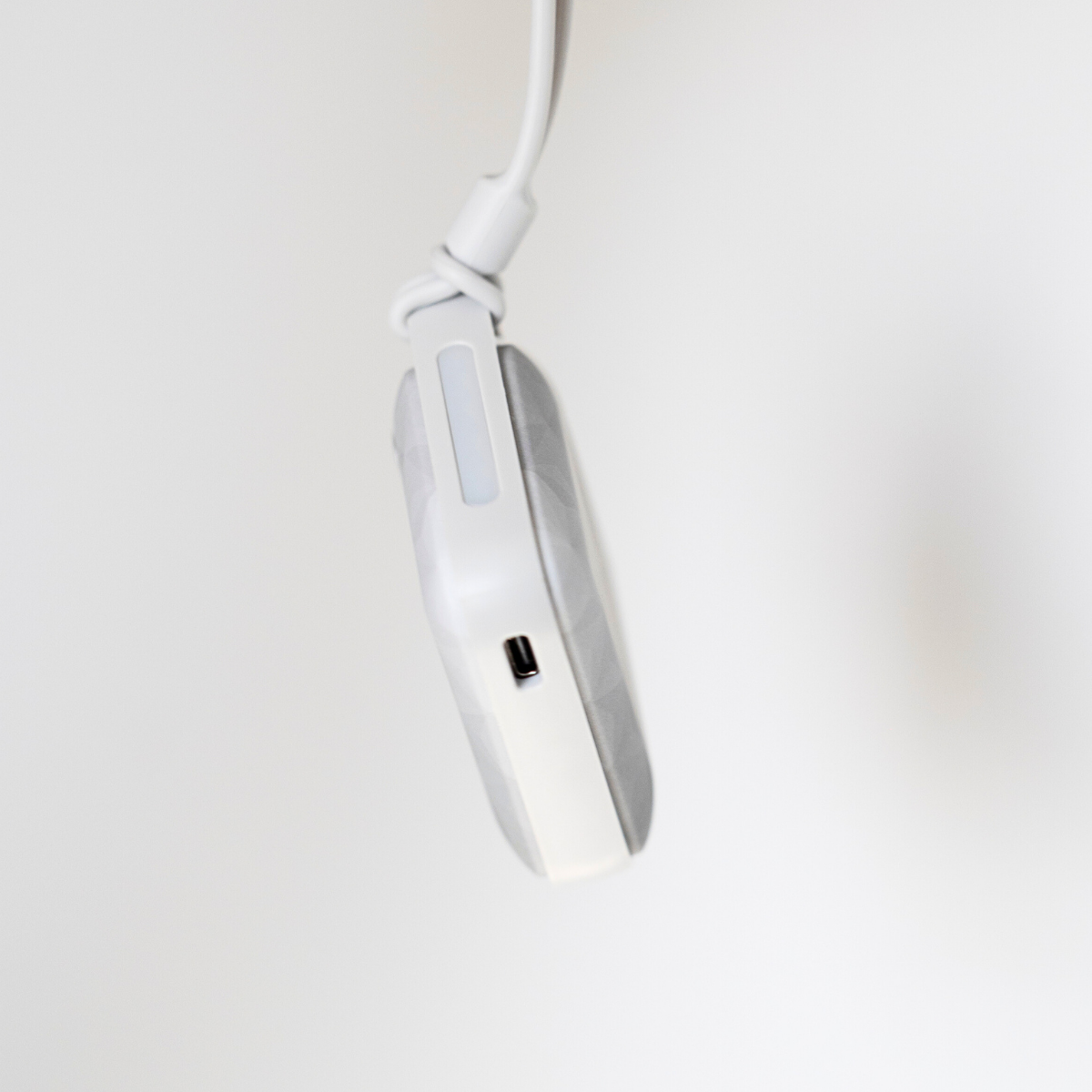 The Charcoal colored USB Rechargeable Handwarmer danging from the wrist strap to display the cable port and LED light