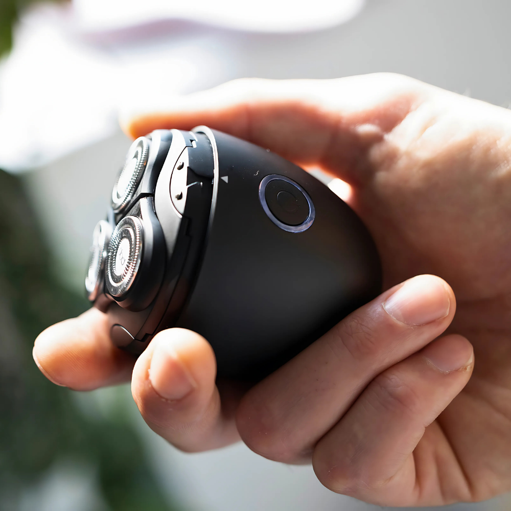 Hand holding a black electric shaver with a blurred background