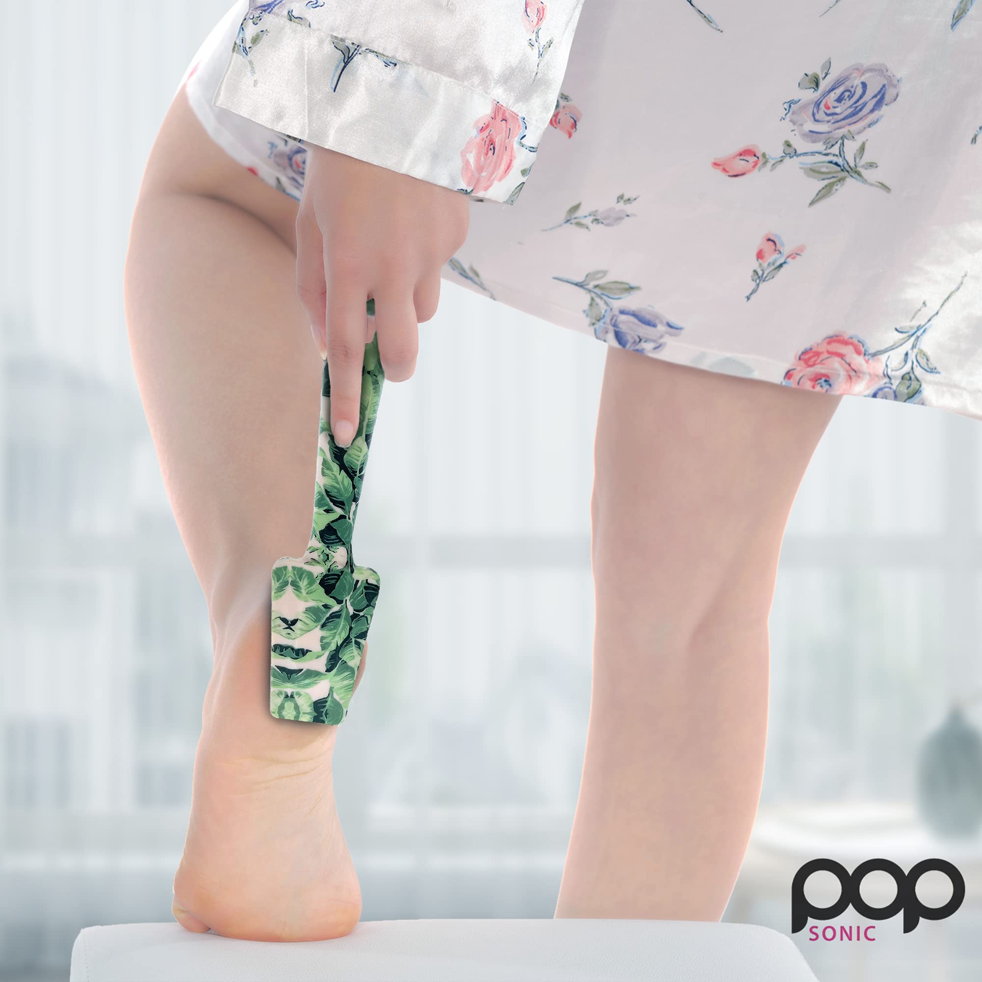 Person wearing a floral dress with a Tropical-patterned Glass Foot File, against a blurred indoor background.