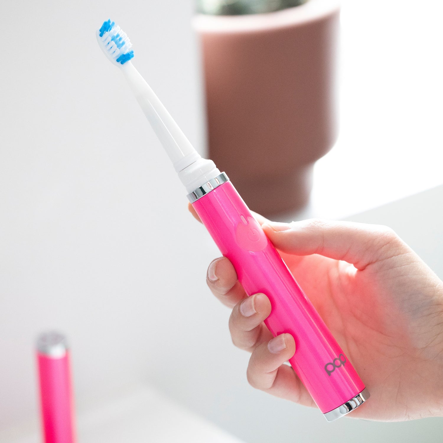 Hand holding a pink electric toothbrush with a blurred background