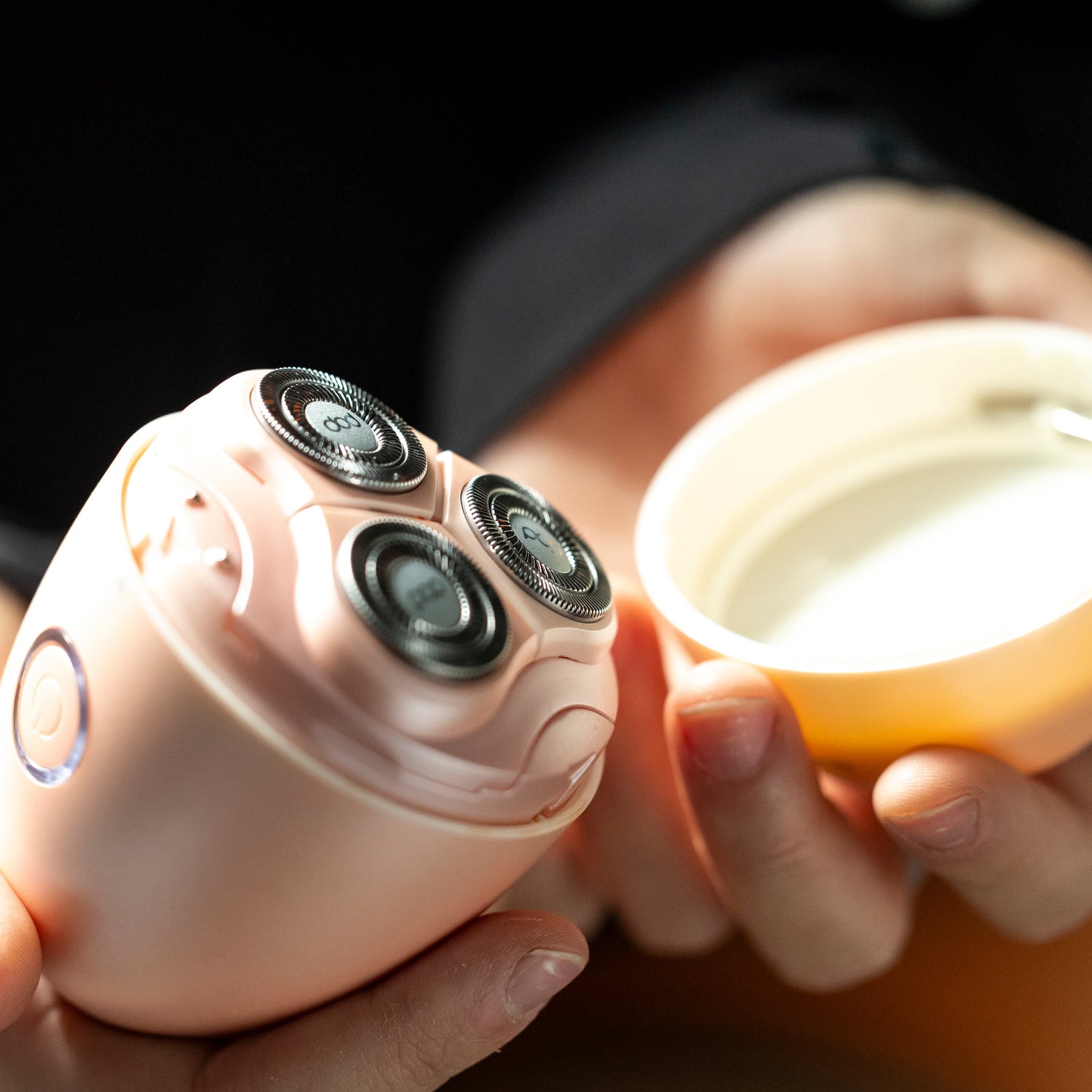 Person holding a pink electronic shaver with 3 round blades and a cap