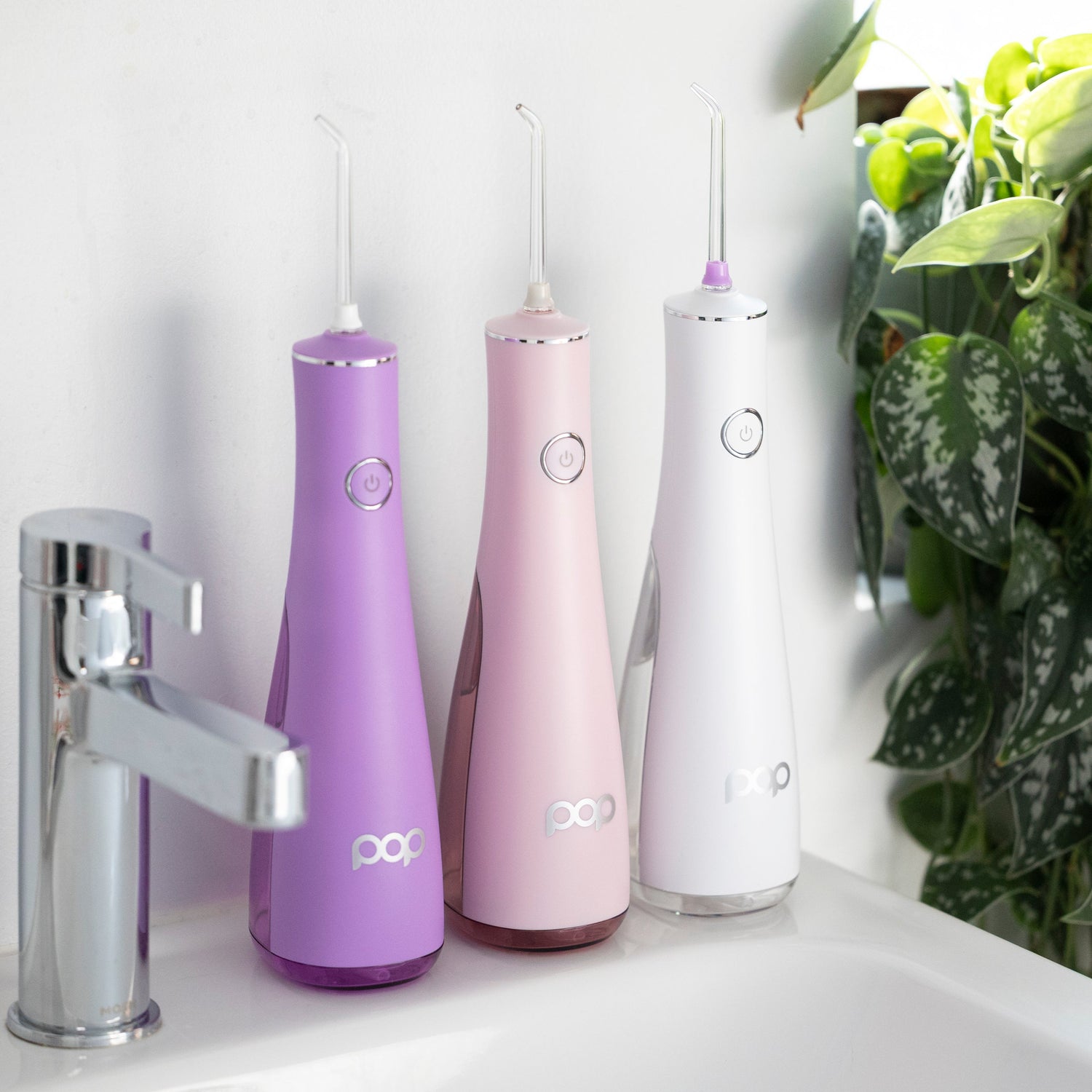 Three dental water flossers on a bathroom counter with a sink and plant in the background.