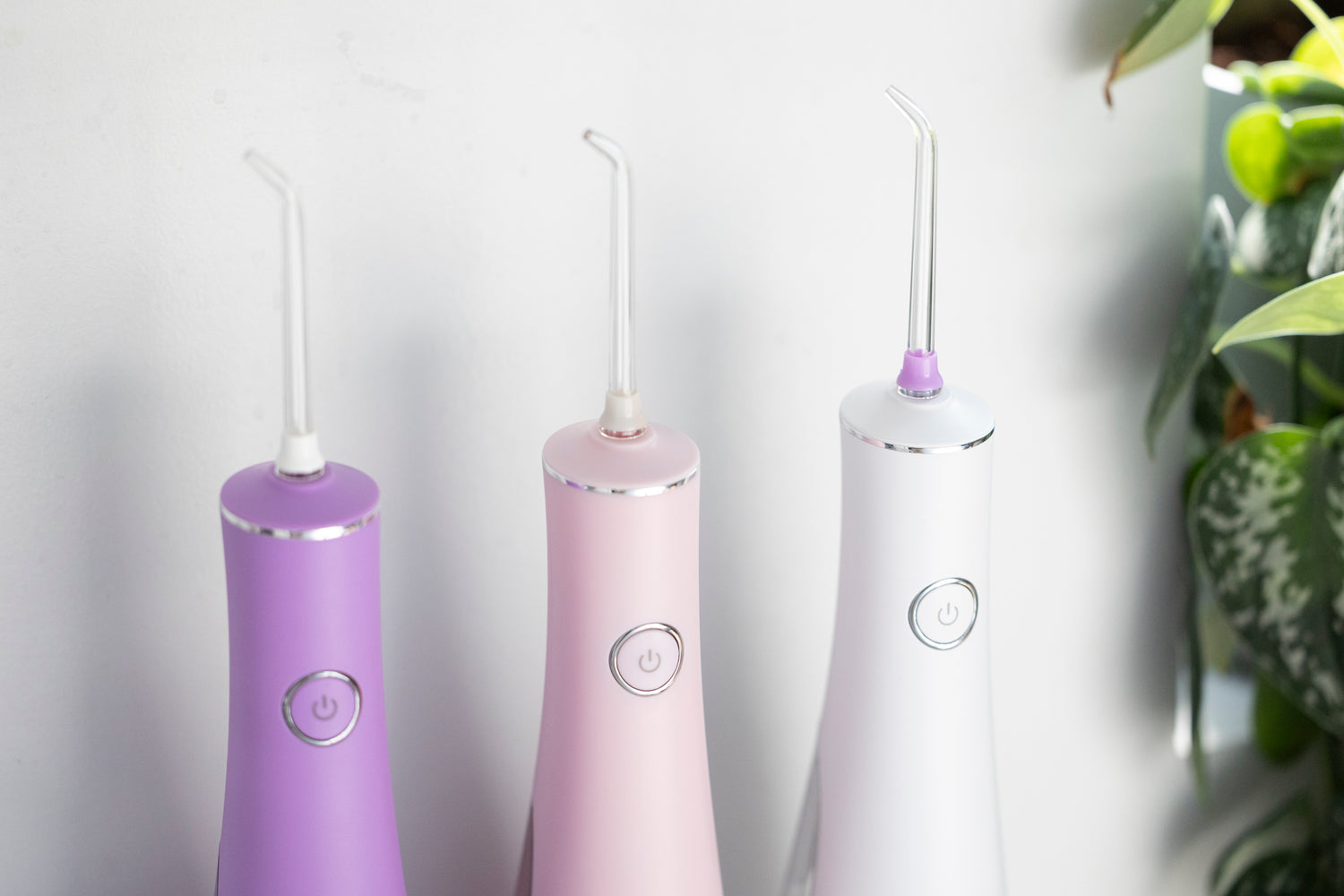 Three dental water flossers in purple, pink, and white on a light gray background.