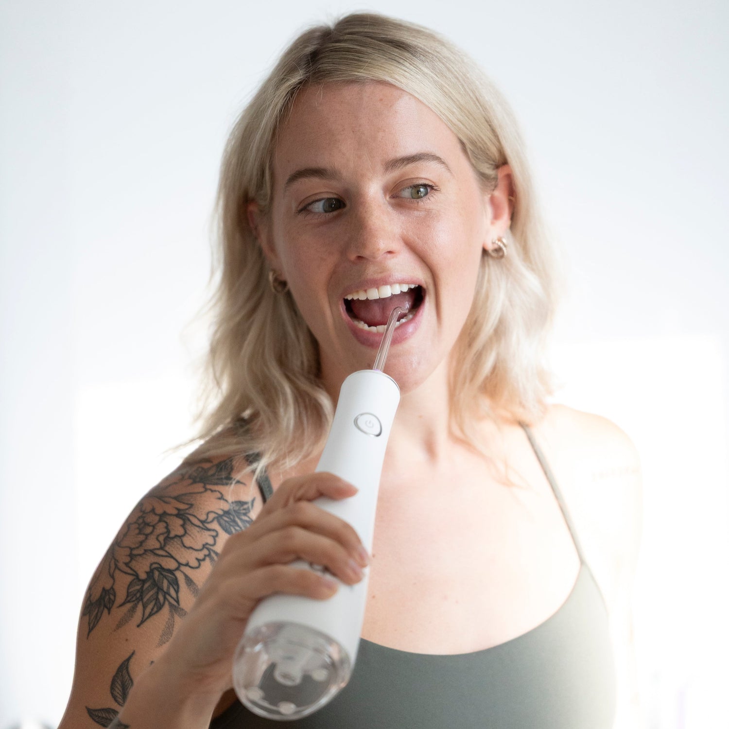 Woman using a white handheld water flosser with a neutral background