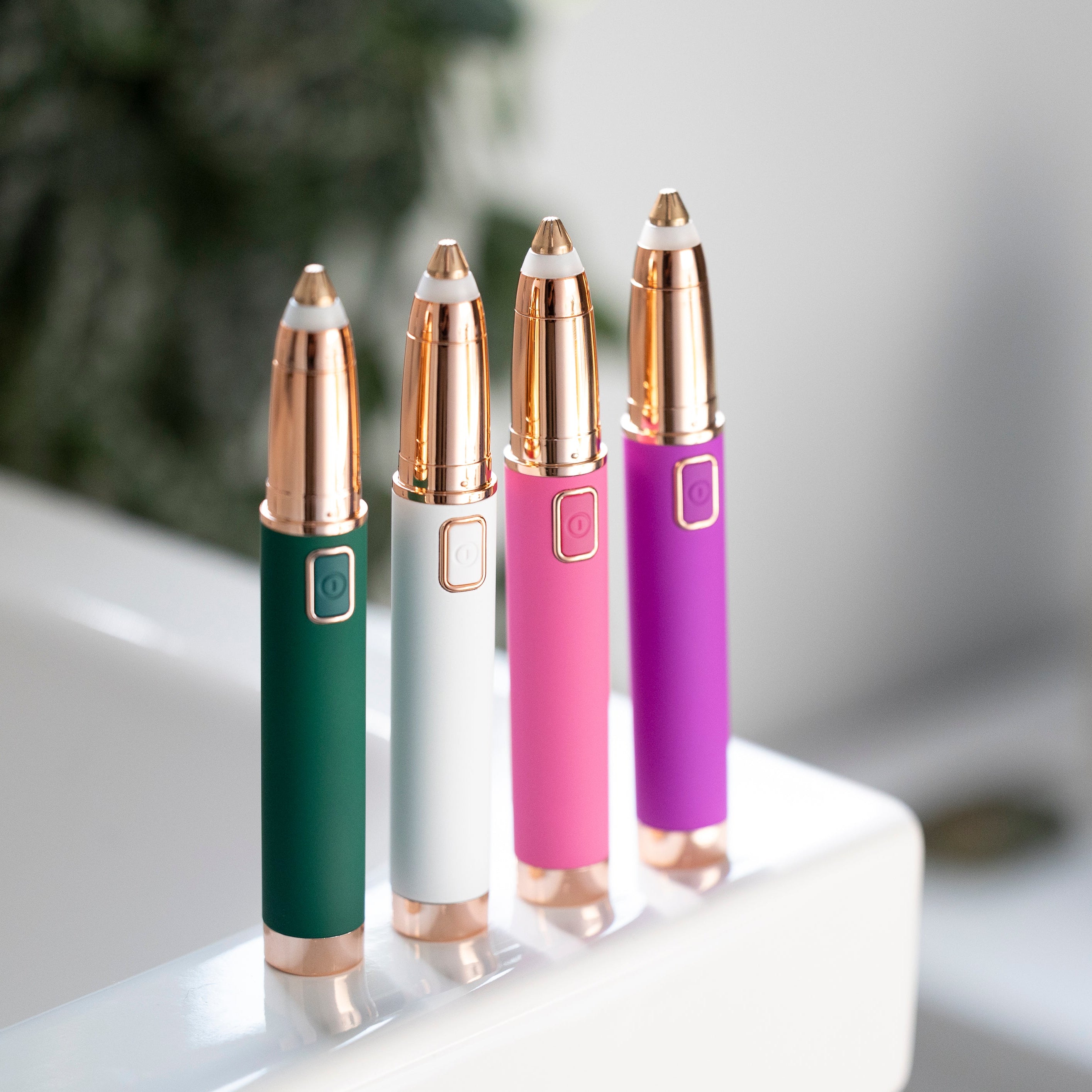 A zoomed out image of all 4 eyebrow shapers on a bathroom counter in green, white, pink, and purple.