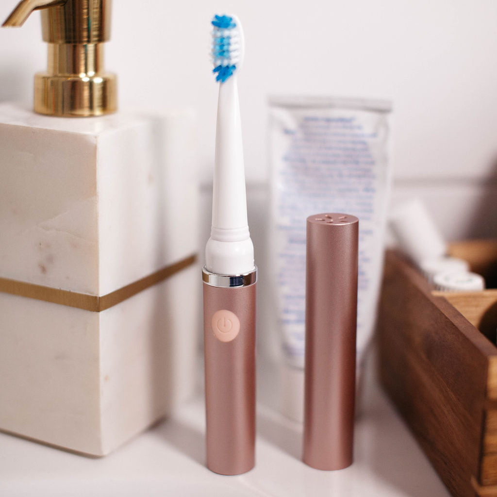 Rose gold electric toothbrush on a bathroom counter with a white background