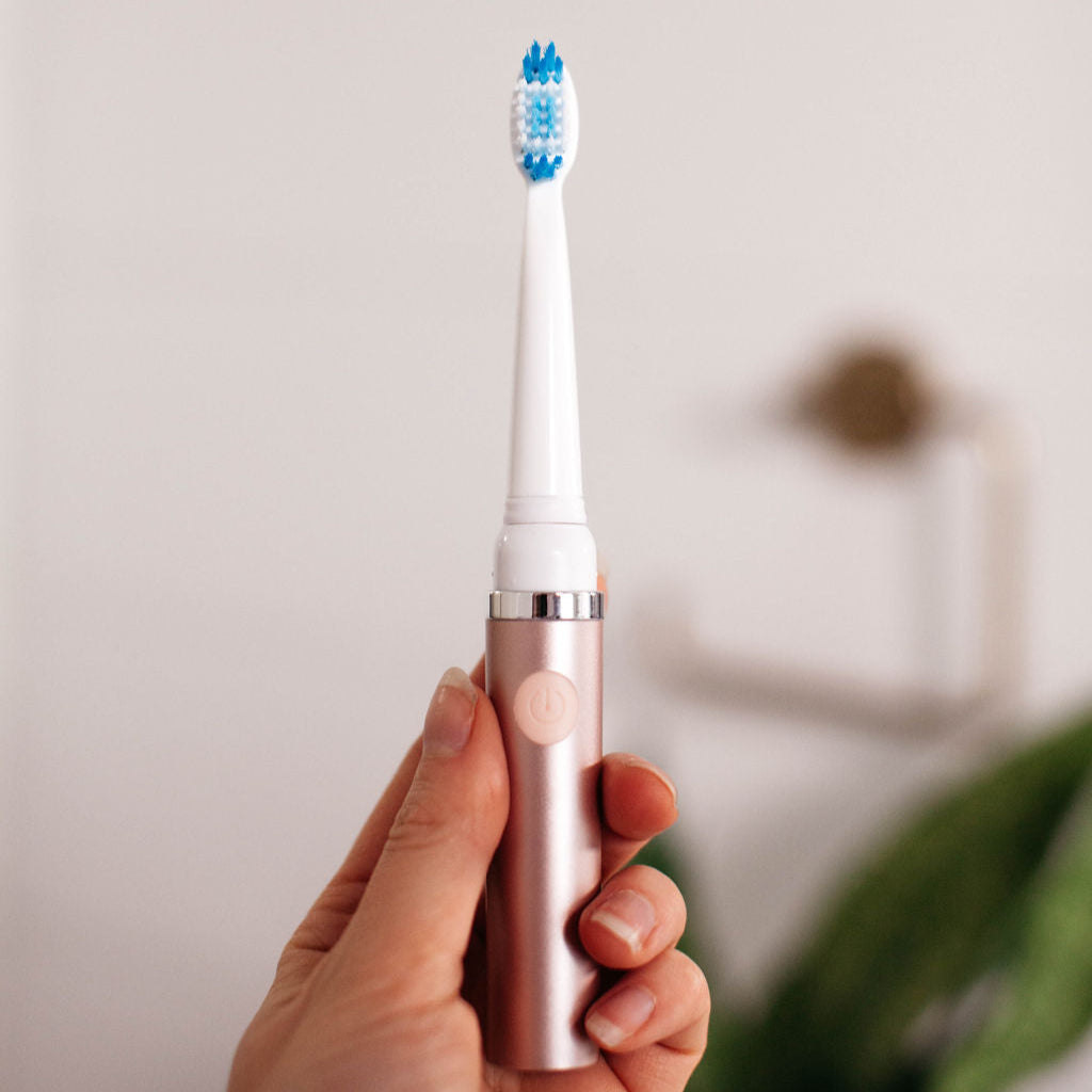 Hand holding a rose gold electric toothbrush with a blurred background