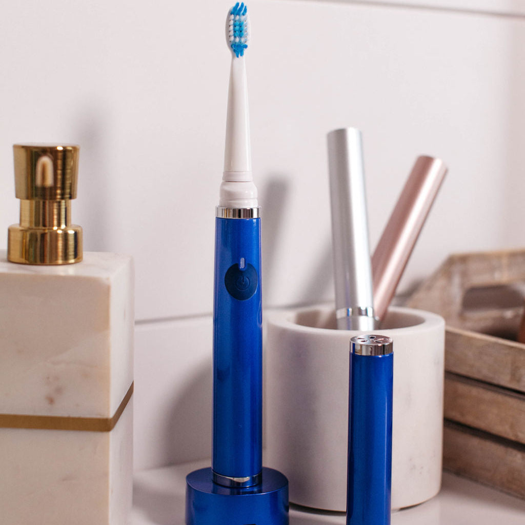 Blue electric toothbrush on a bathroom counter with a white container and other items.