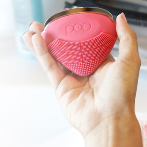 Pink silicone exfoliating device held in a hand with a blurred background