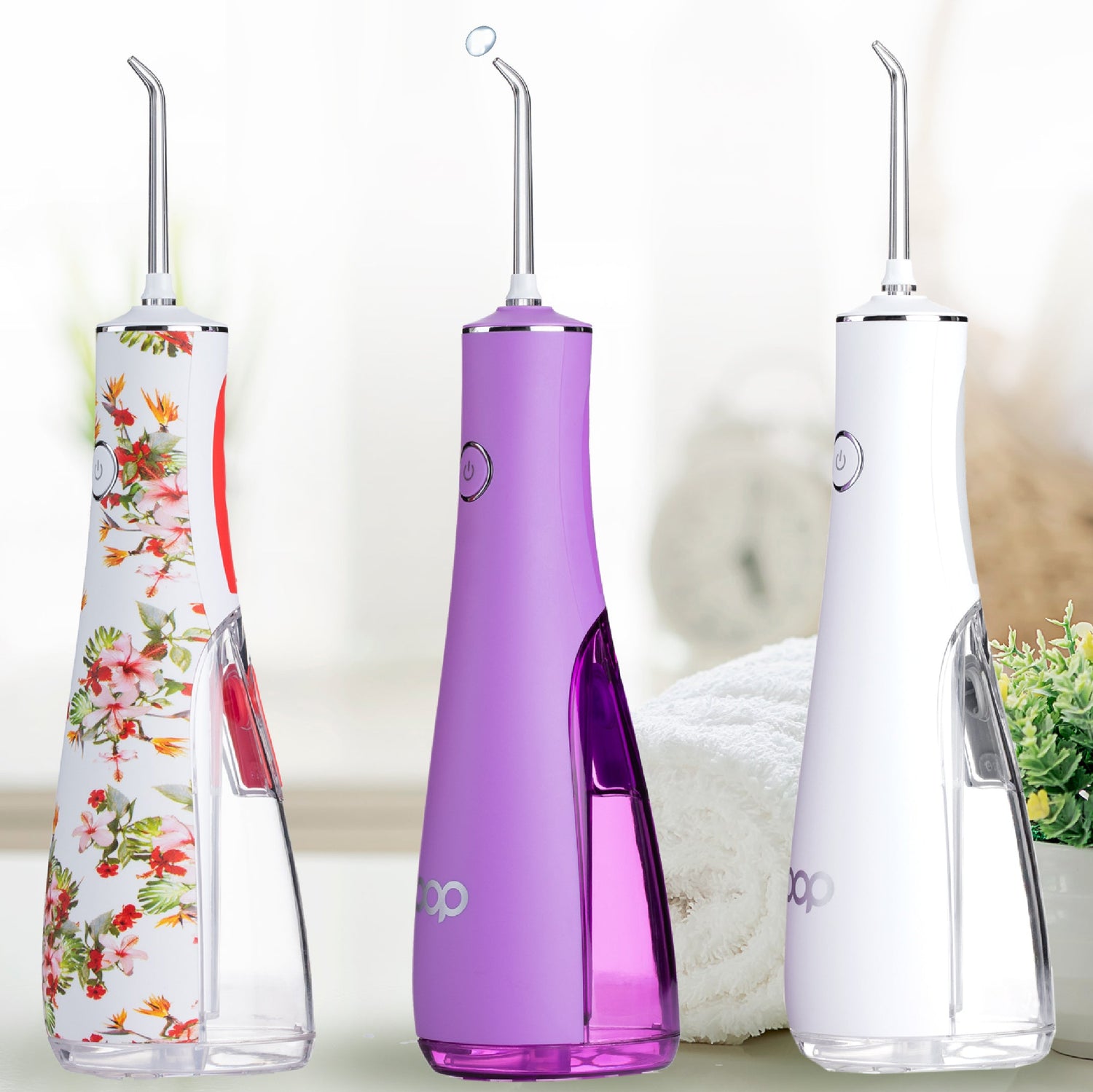 Three dental water flossers in botanical-pattern, purple, and white with a n indoor bathroom and towel in the background
