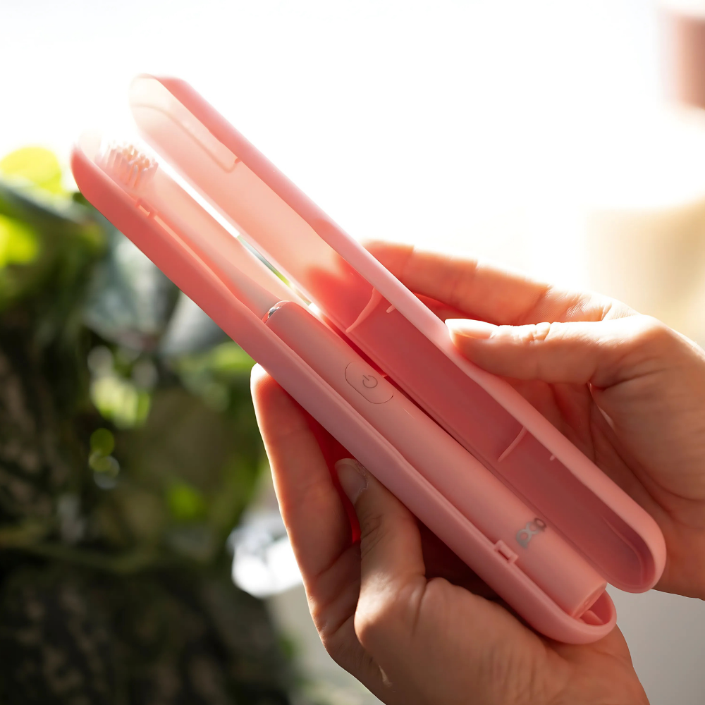 Person holding a pink toothbrush in a pink case with a blurred green plant in the background