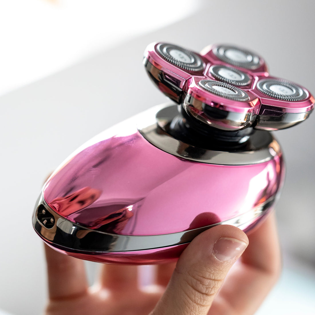 Hand holding a pink, five-blade electric shaver with a blurred 