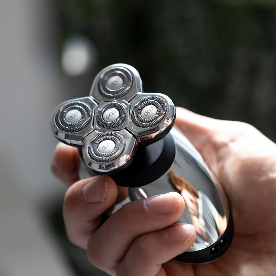 Hand holding a silver, five-blade electric shaver with a blurred background