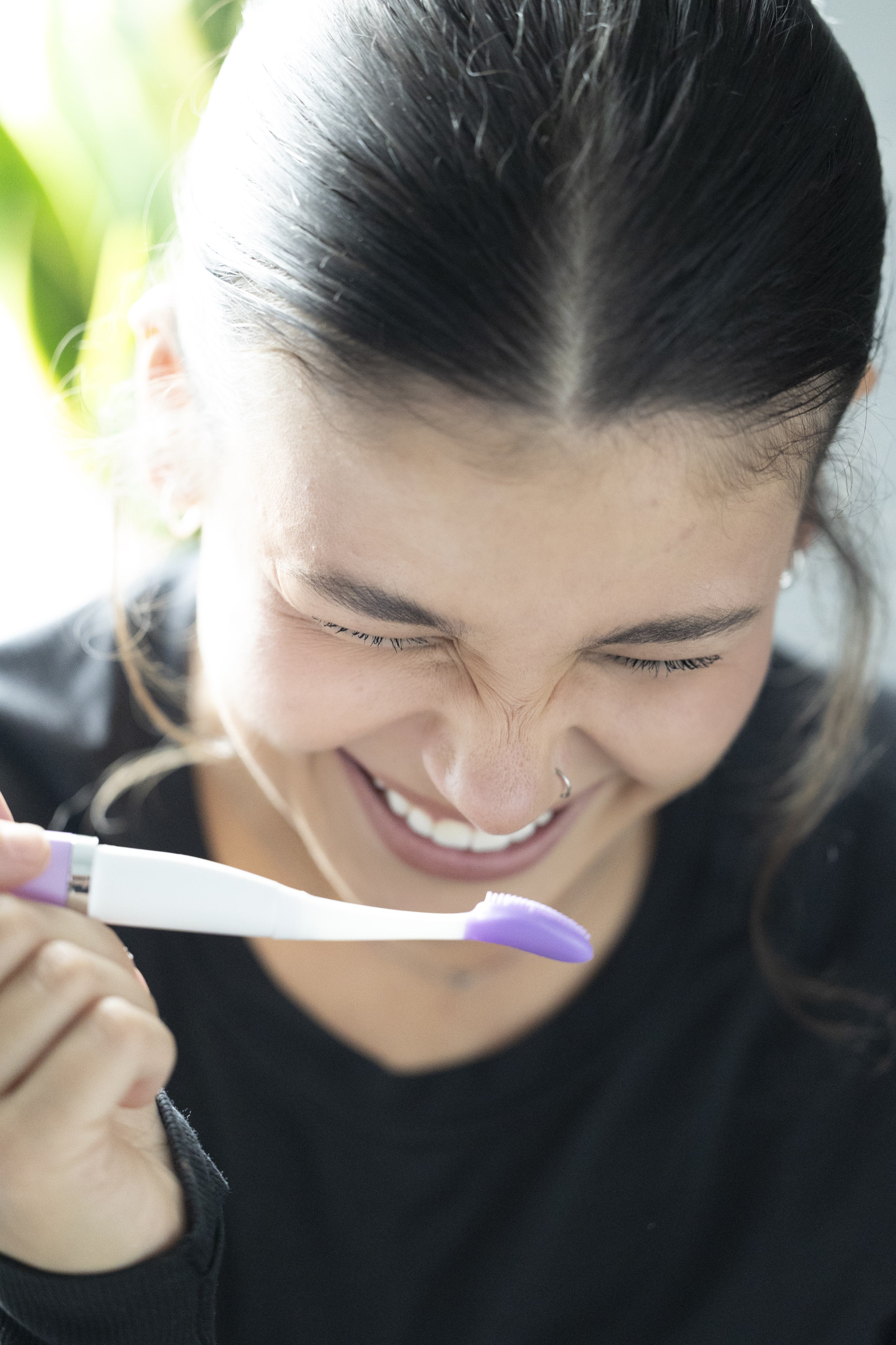 Girl with dark brown hair laughing with a purple and white lip exfoliating tool in her hand