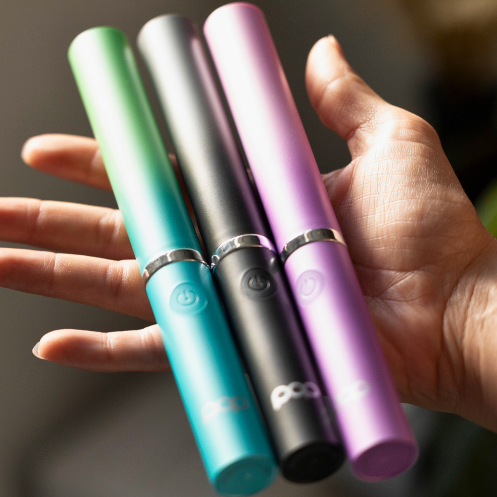 Three colorful toothbrushes in Blue Ombre, Black Ombre, and Purple Ombre held in a hand against a blurred background